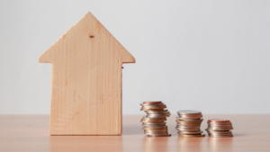 Image of a scale with a wooden home on one side and coins on the other, indicating the balance of mortgage rates and refinancing.