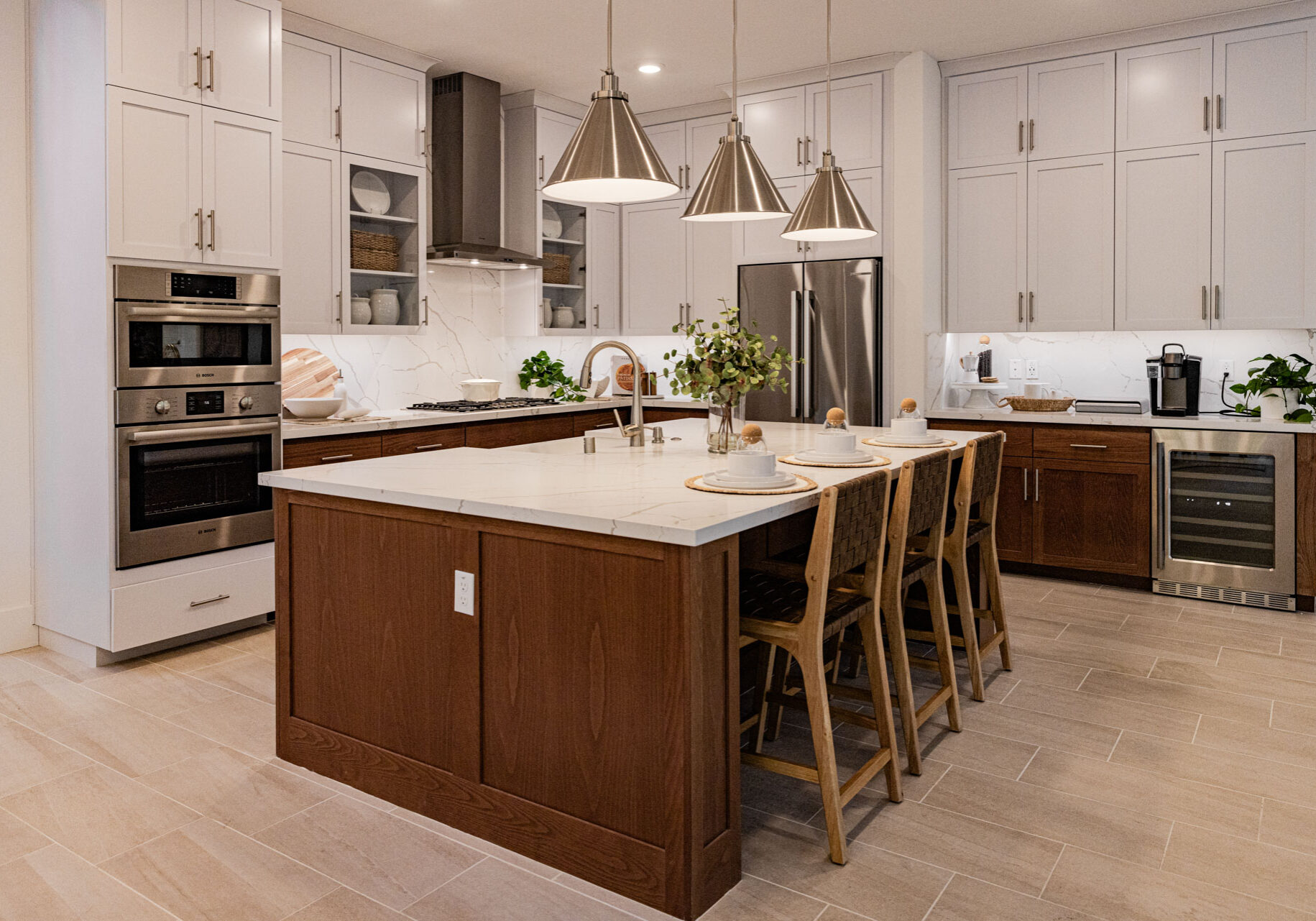 The_Woods-Res4-07 Large kitchen island with wood paneling and marble countertop with white cabinetry and stainless steel appliance in the background.
